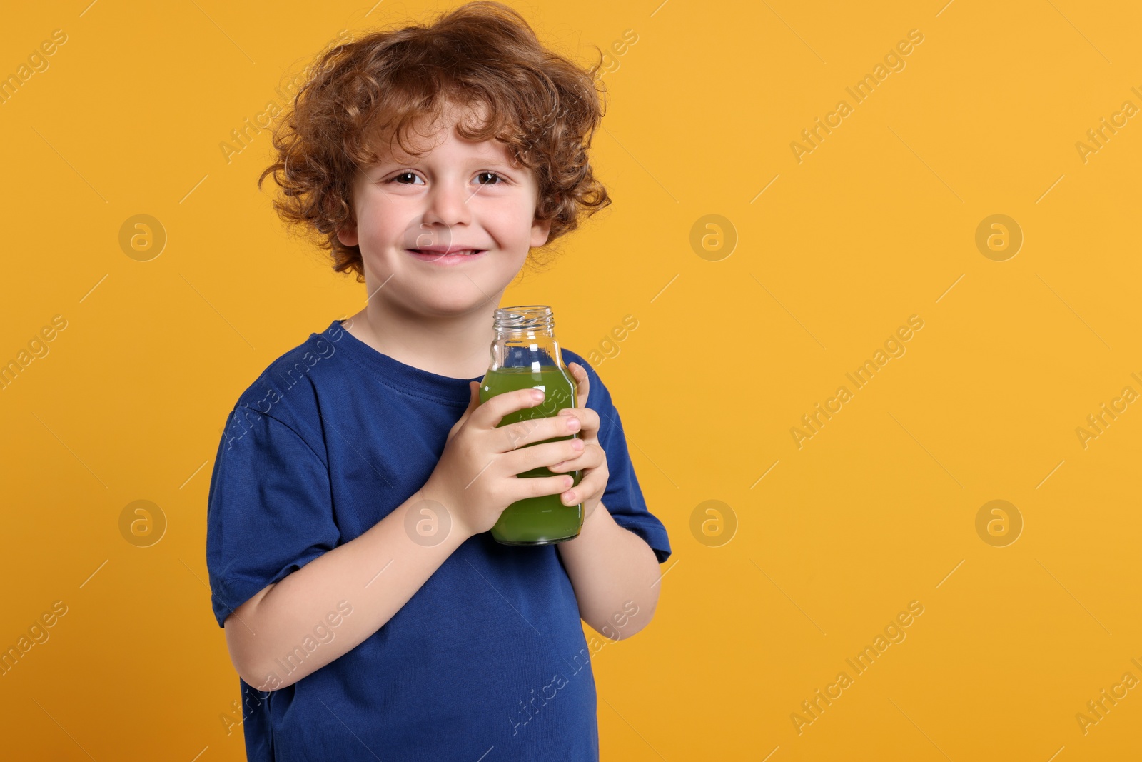 Photo of Cute little boy with glass bottle of fresh juice on orange background, space for text