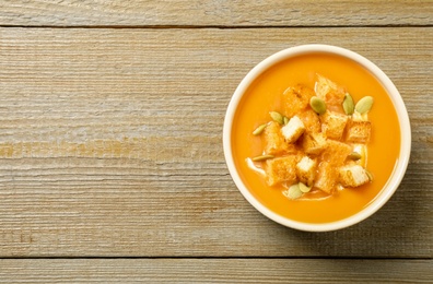 Photo of Tasty creamy pumpkin soup with croutons and seeds in bowl on wooden table, top view. Space for text