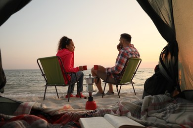 Photo of Couple resting near sea at sunset, view from camping tent