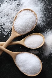 Photo of Organic salt in spoons on black table, flat lay