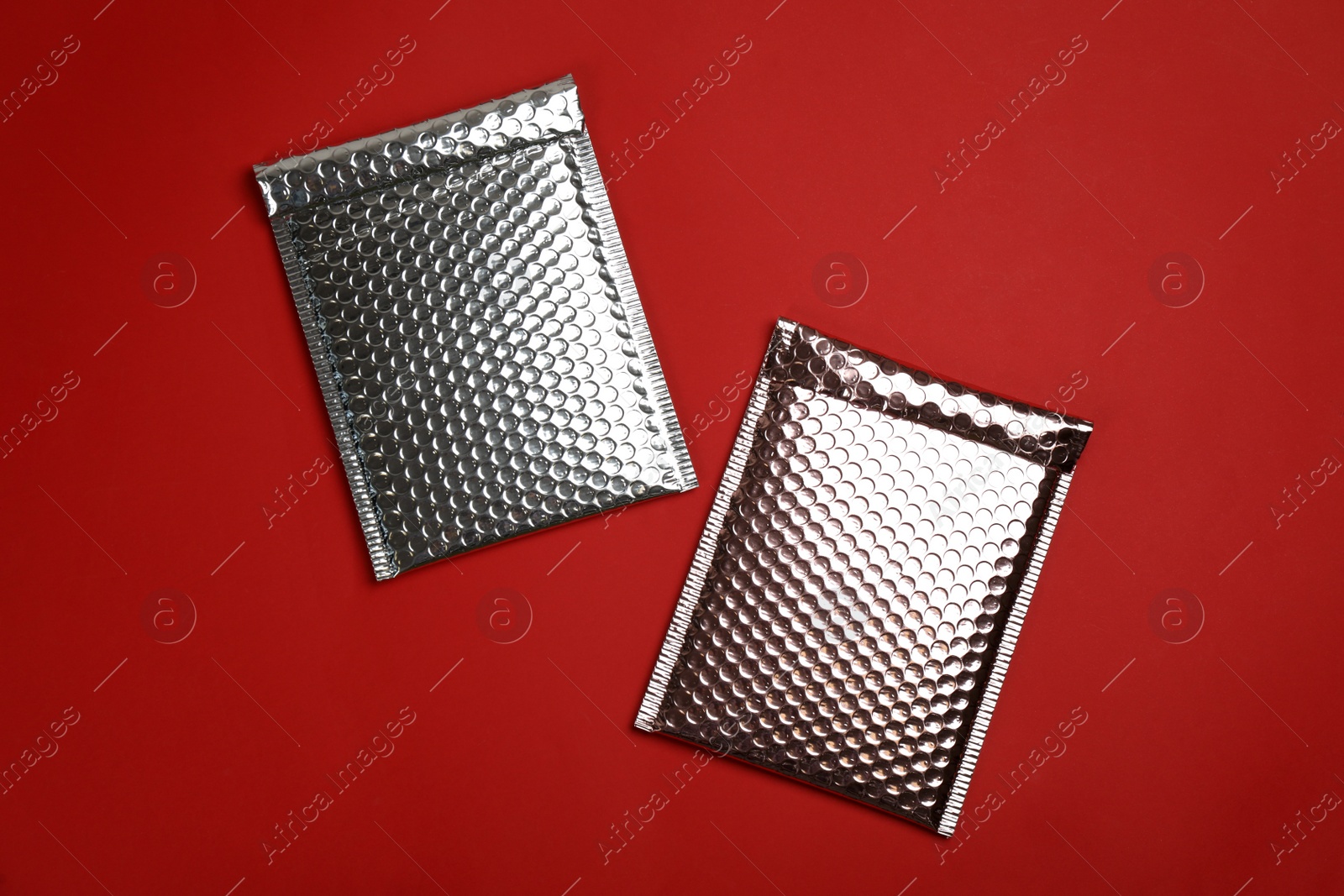 Photo of Two padded envelopes with bubble wrap on red background, flat lay