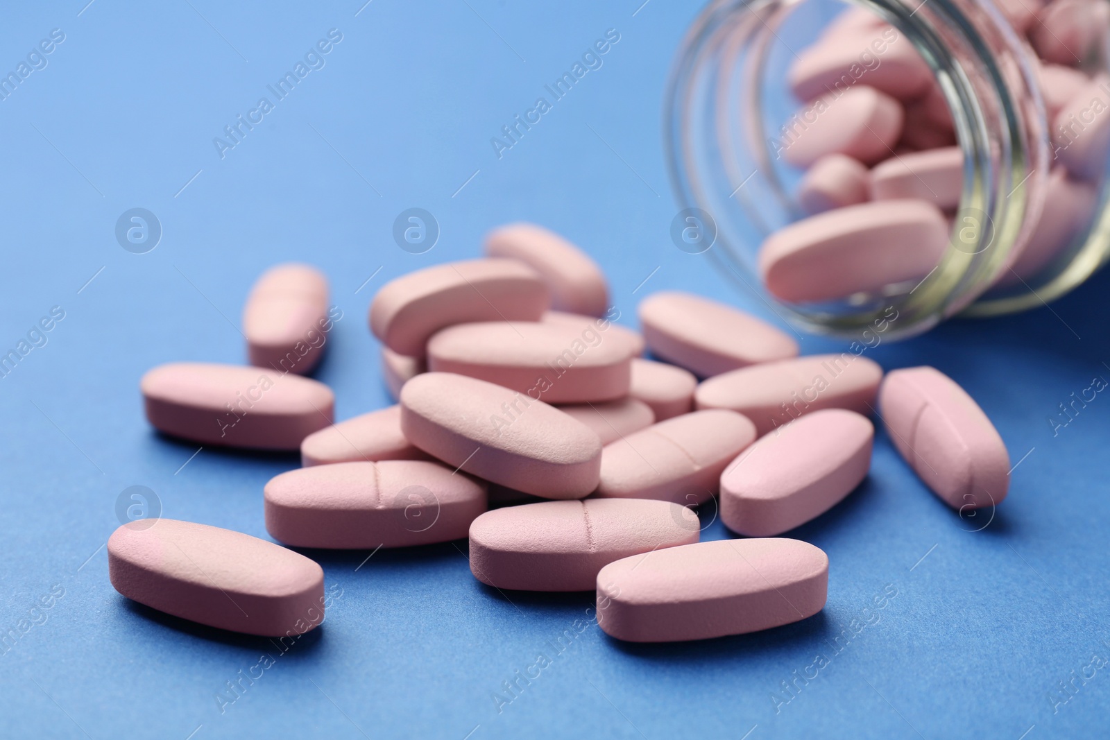 Photo of Bottle of pink vitamin capsules on blue background, closeup