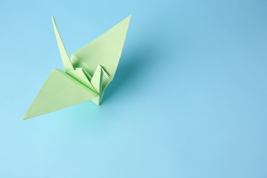Photo of Origami art. Handmade paper crane on light blue background, above view. Space for text
