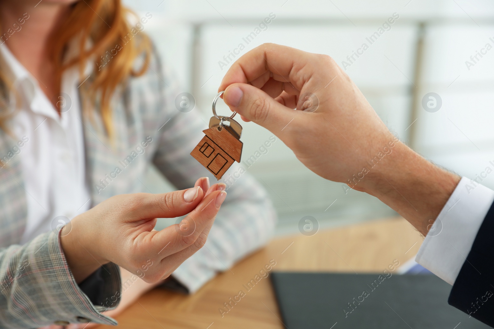 Photo of Real estate agent giving key with trinket to client in office, closeup