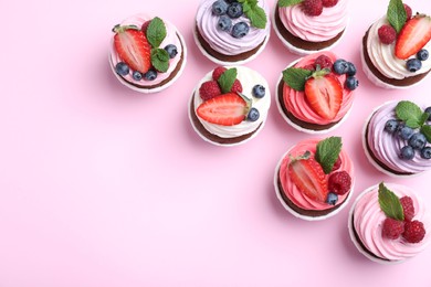 Photo of Different delicious cupcakes with cream and berries on pink background, flat lay. Space for text