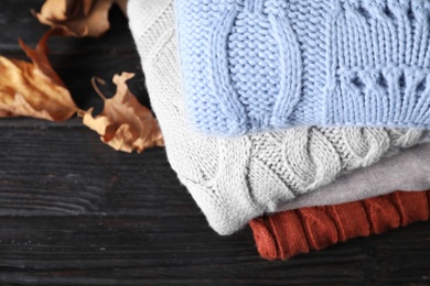 Stack of folded warm sweaters and dry leaves on black wooden table, above view