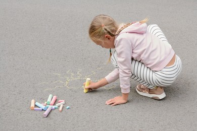 Photo of Little child drawing sun with chalk on asphalt