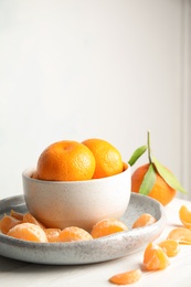 Photo of Plate and bowl with ripe tangerines on table