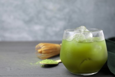 Glass of delicious iced green matcha tea on grey wooden table, closeup. Space for text