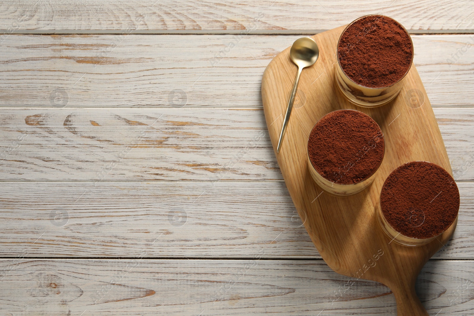 Photo of Delicious tiramisu in glasses and spoon on light wooden table, top view. Space for text