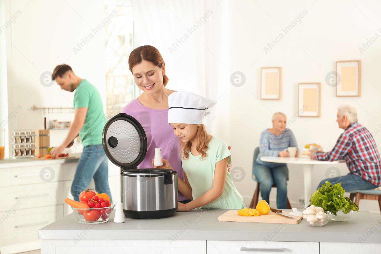 Photo of Mother and daughter preparing food with modern multi cooker in kitchen