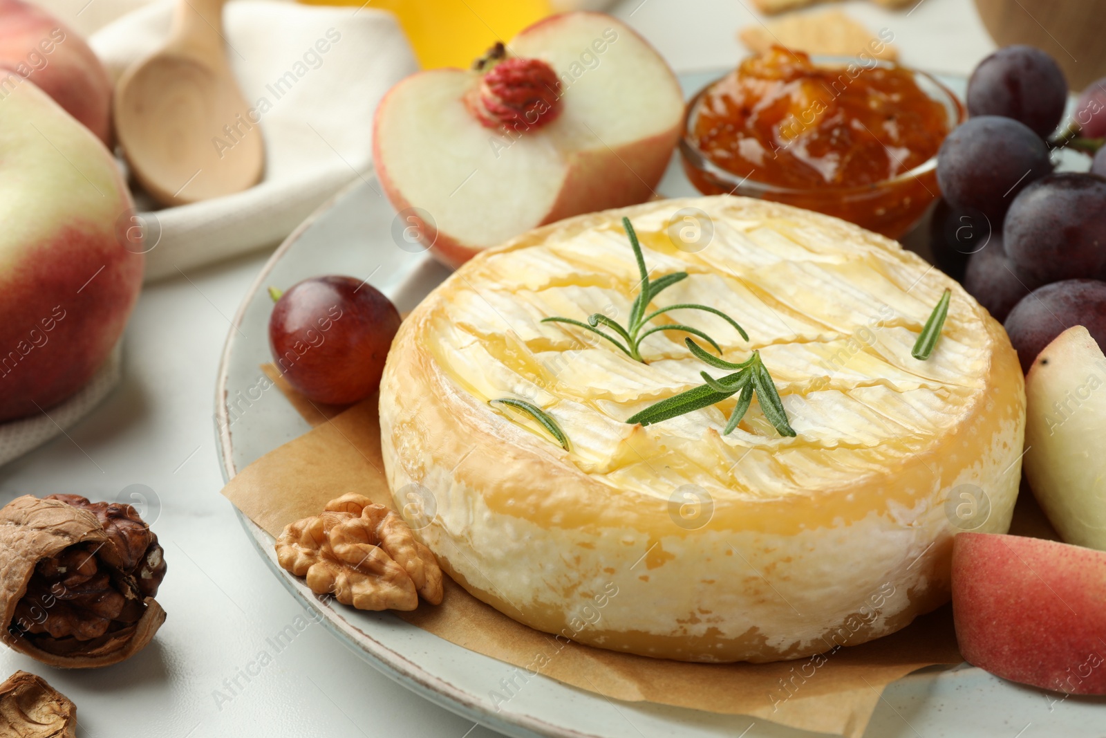 Photo of Tasty baked brie cheese with rosemary, fruits and walnuts on white table, closeup