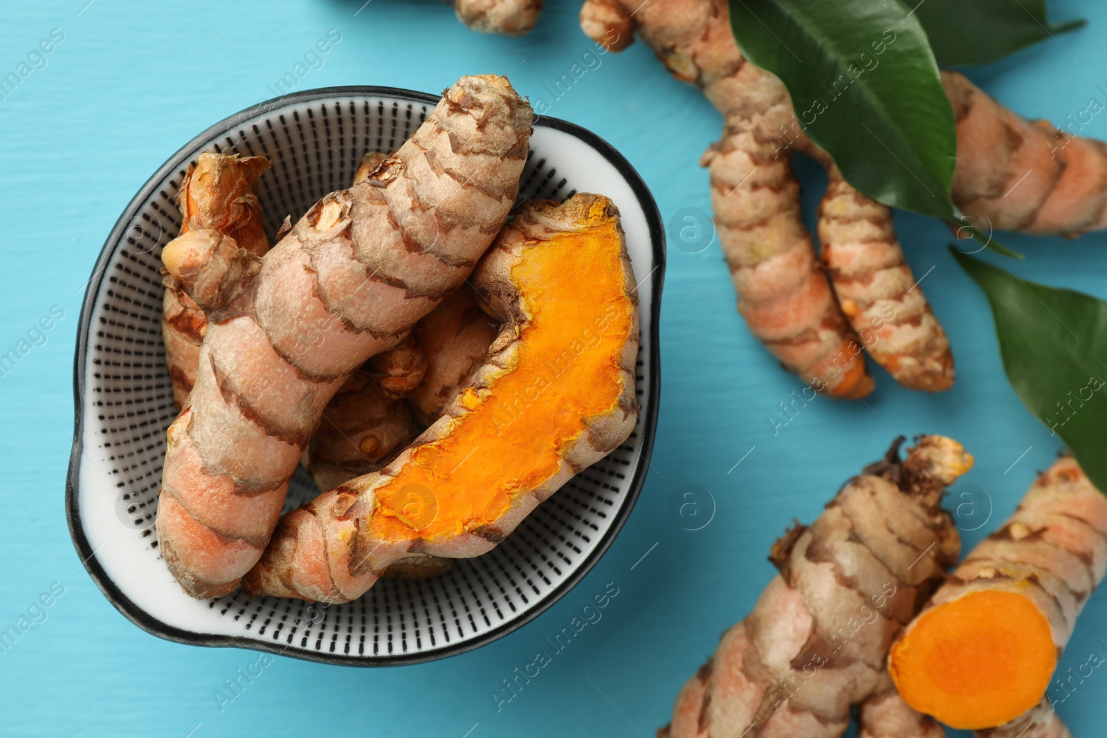 Photo of Whole and cut turmeric roots on light blue wooden table, flat lay