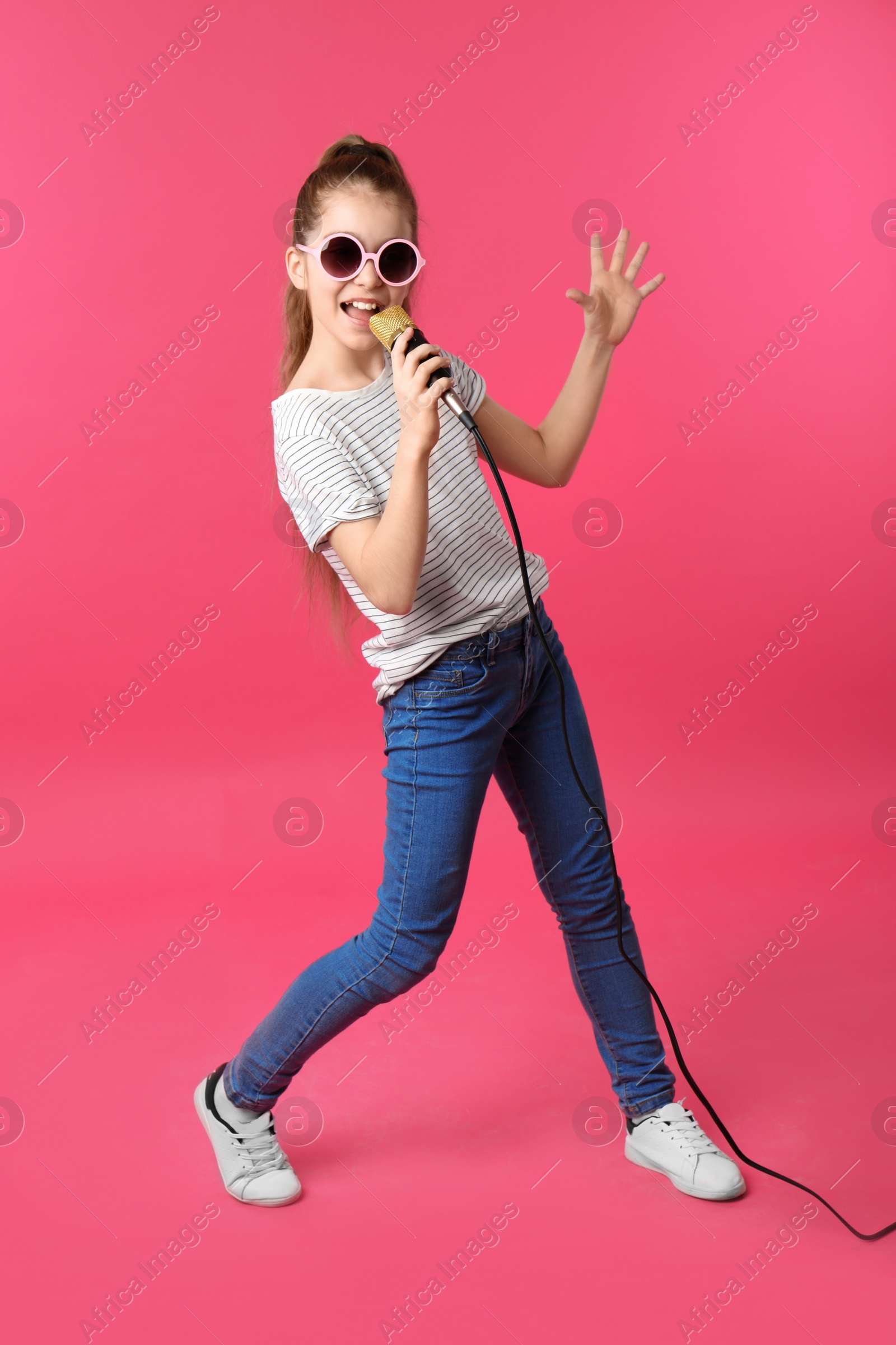 Photo of Cute girl singing in microphone on color background