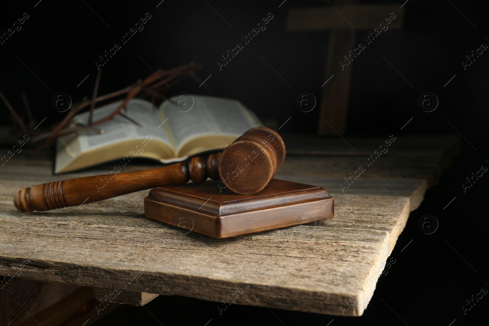 Photo of Judge gavel, bible, cross and crown of thorns on wooden table against black background