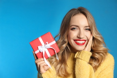 Happy young woman with Christmas gift on light blue background