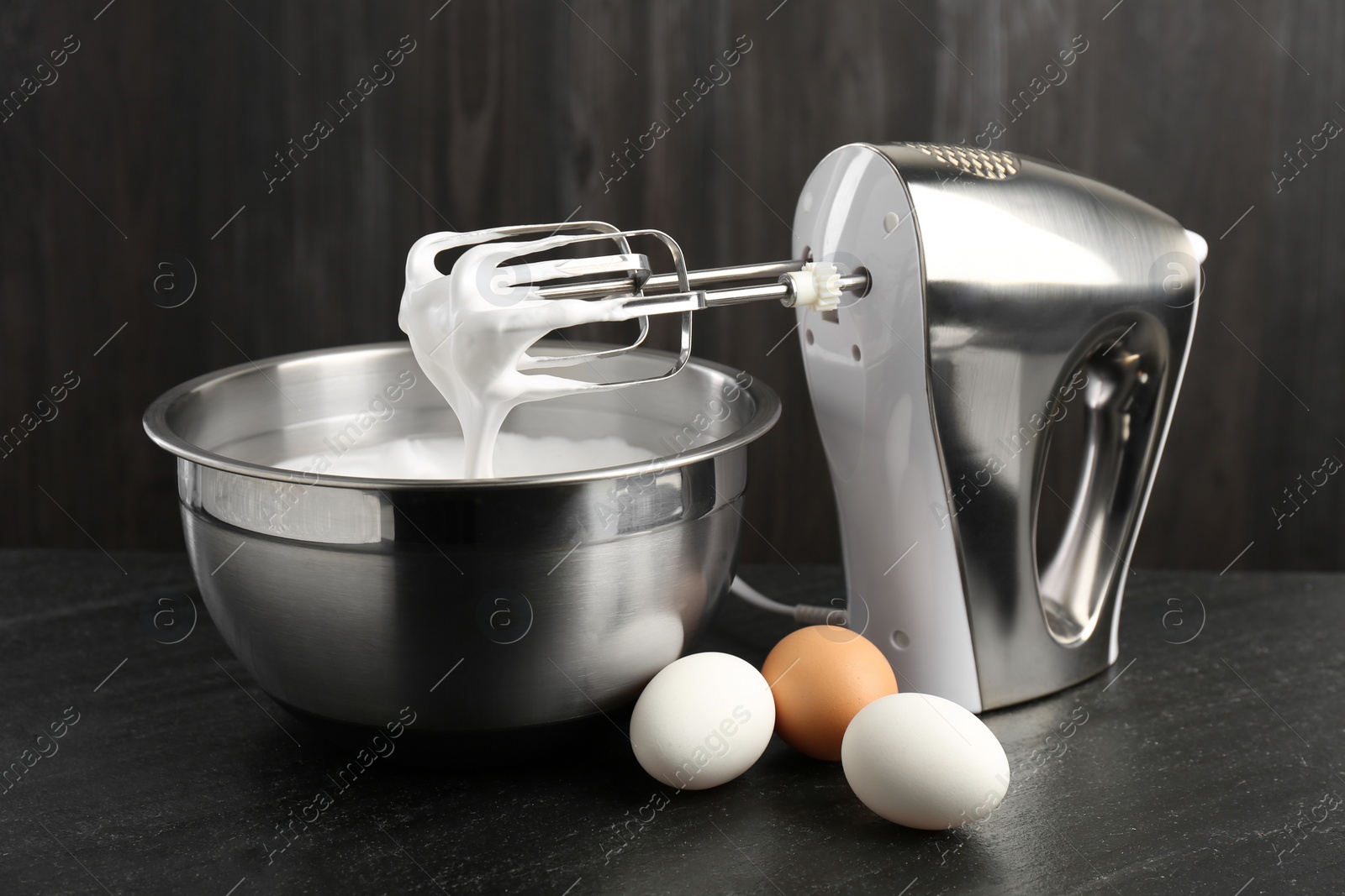 Photo of Bowl with whipped cream, hand mixer and eggs on black table