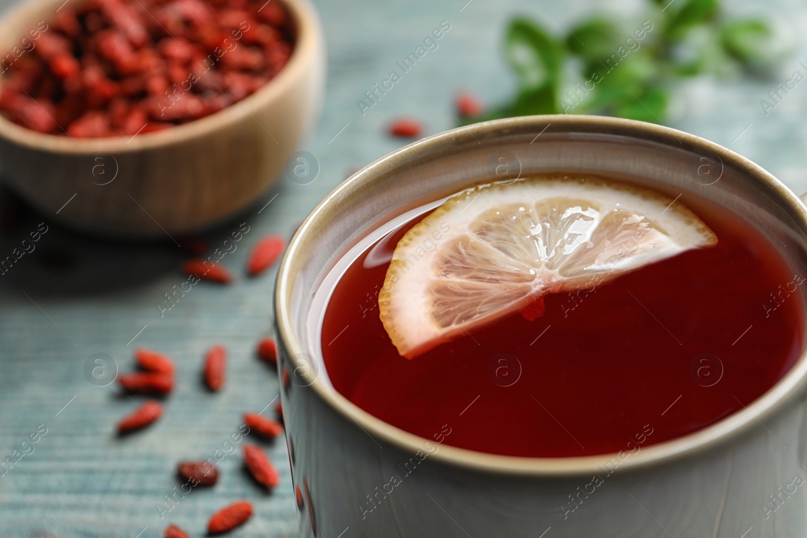 Photo of Healthy goji tea with lemon in cup on blue wooden table, closeup