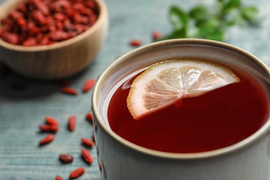 Photo of Healthy goji tea with lemon in cup on blue wooden table, closeup