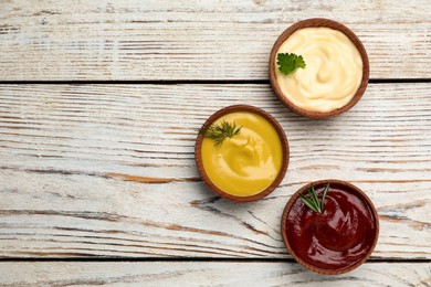 Photo of Bowls with mustard, ketchup and mayonnaise on wooden table, flat lay. Space for text