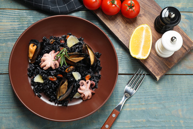 Photo of Delicious black risotto with seafood served on blue wooden table, flat lay