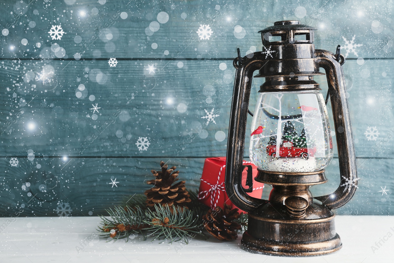 Image of Beautiful Christmas snow globe in vintage lantern on light blue wooden background, bokeh effect. Space for text