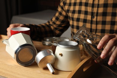 Brewing coffee. Man pouring water into moka pot at table indoors, closeup