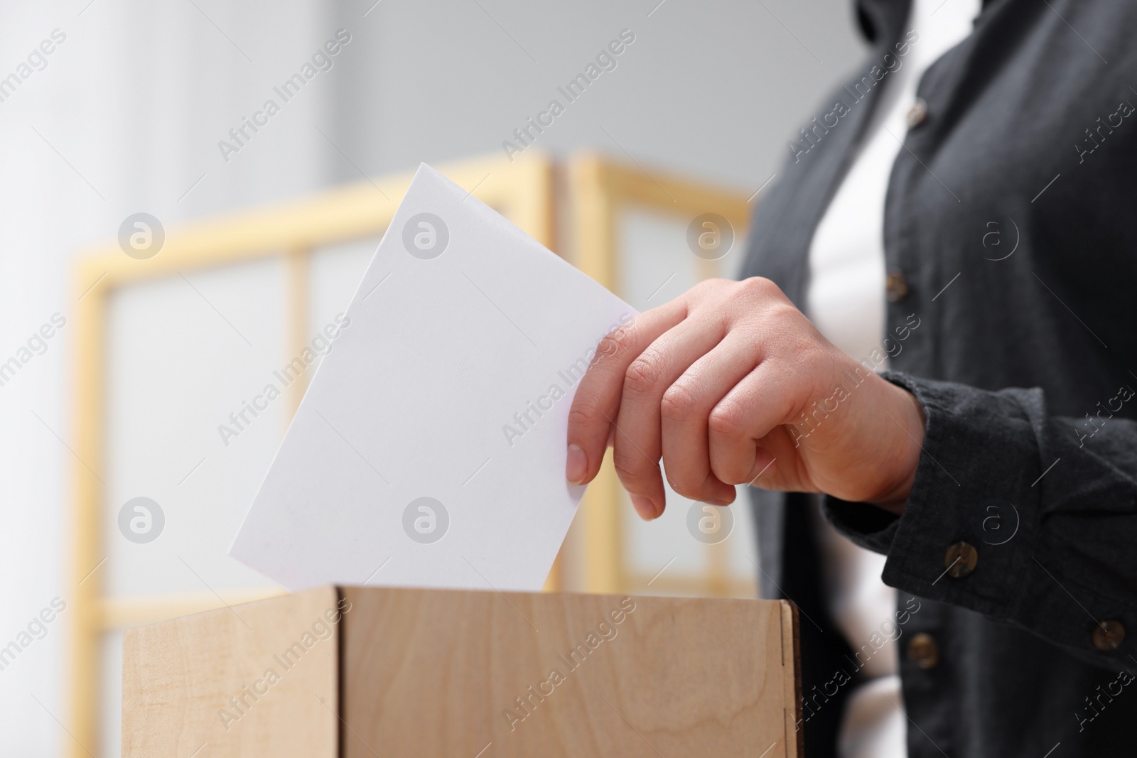 Photo of Woman putting her vote into ballot box on blurred background, closeup