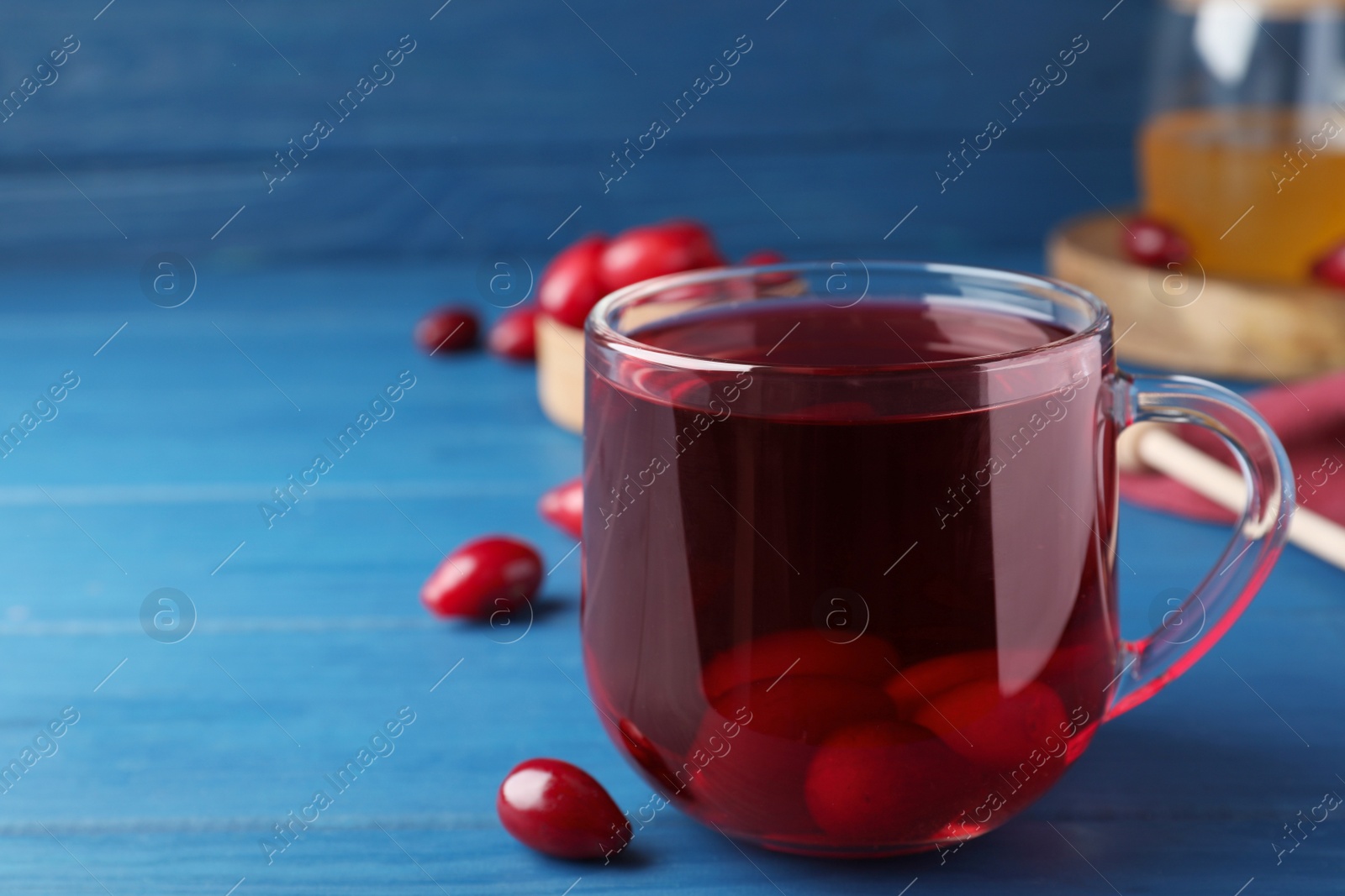 Photo of Glass cup of fresh dogwood tea with berries on blue wooden table. Space for text