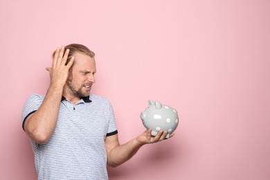 Emotional man with piggy bank on color background. Space for text