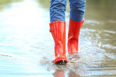 Photo of Woman with red rubber boots in puddle, closeup. Rainy weather