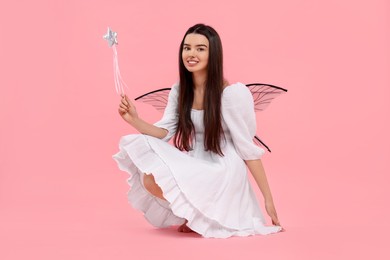 Photo of Beautiful girl in fairy costume with wings and magic wand on pink background