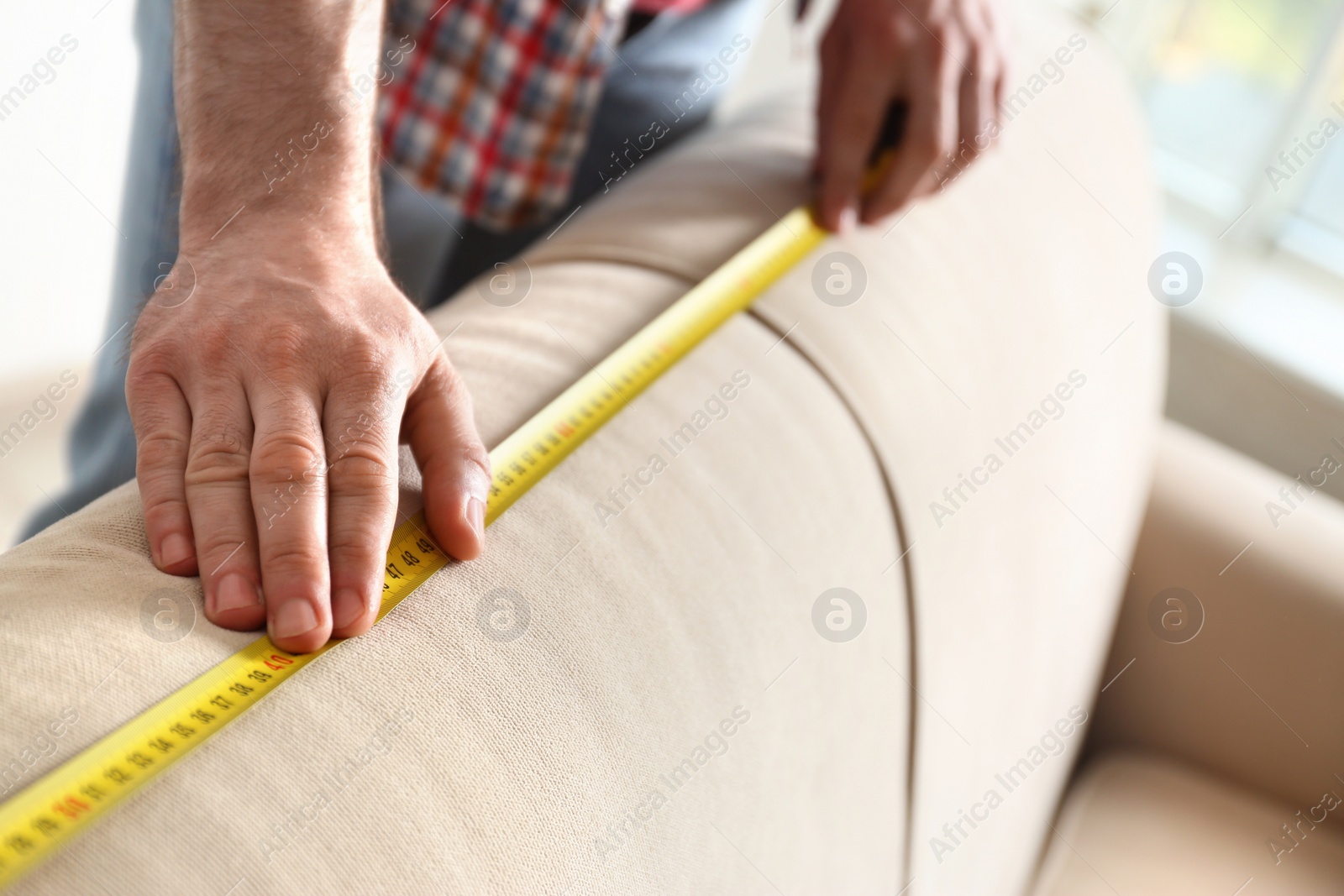Photo of Man measuring beige sofa, closeup. Construction tool