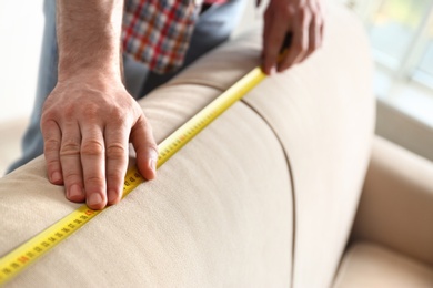 Photo of Man measuring beige sofa, closeup. Construction tool