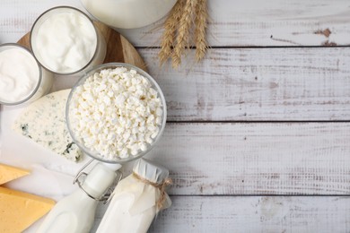 Photo of Different fresh dairy products and wheat ears on white wooden table, flat lay. Space for text