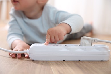 Photo of Little child playing with power strip on floor indoors, closeup. Dangerous situation