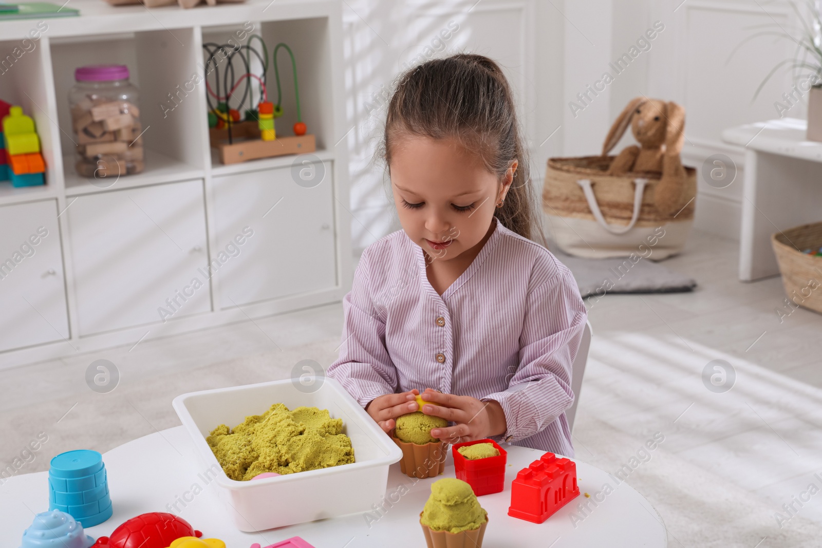 Photo of Cute little girl playing with bright kinetic sand at table in room