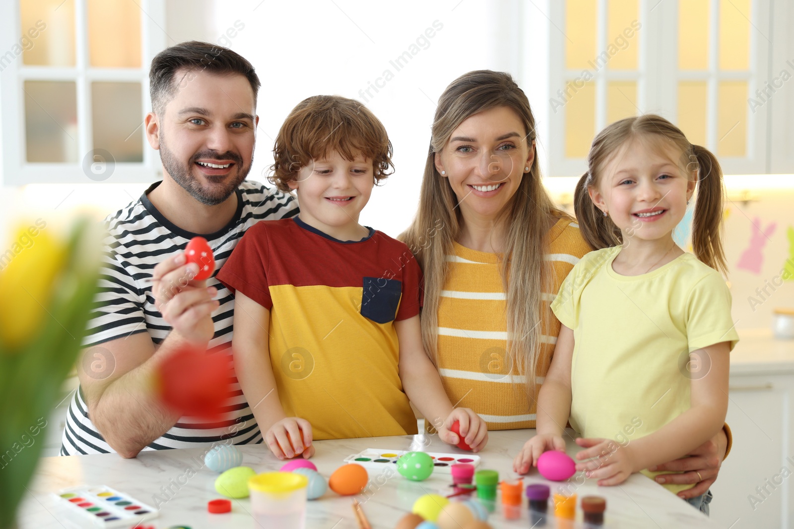 Photo of Easter celebration. Portrait of happy family with painted eggs at white marble table in kitchen