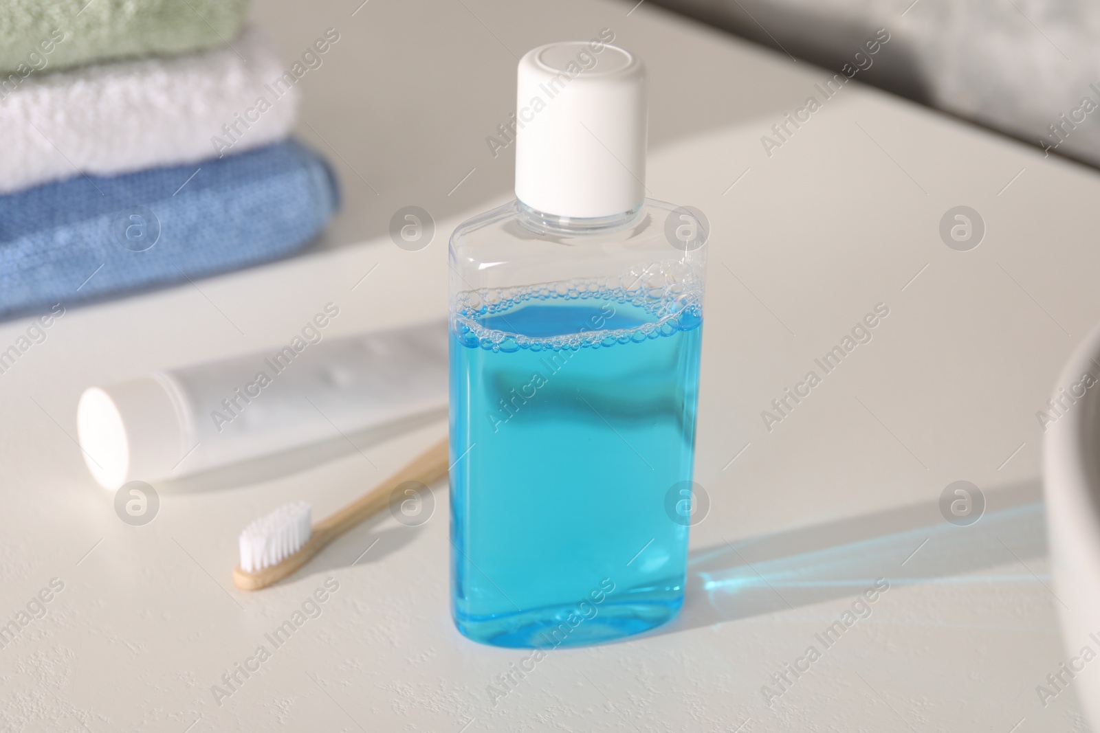Photo of Bottle of mouthwash, toothpaste and toothbrush on white table in bathroom