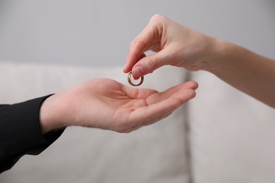 Woman giving wedding ring to her husband indoors, closeup. Divorce concept