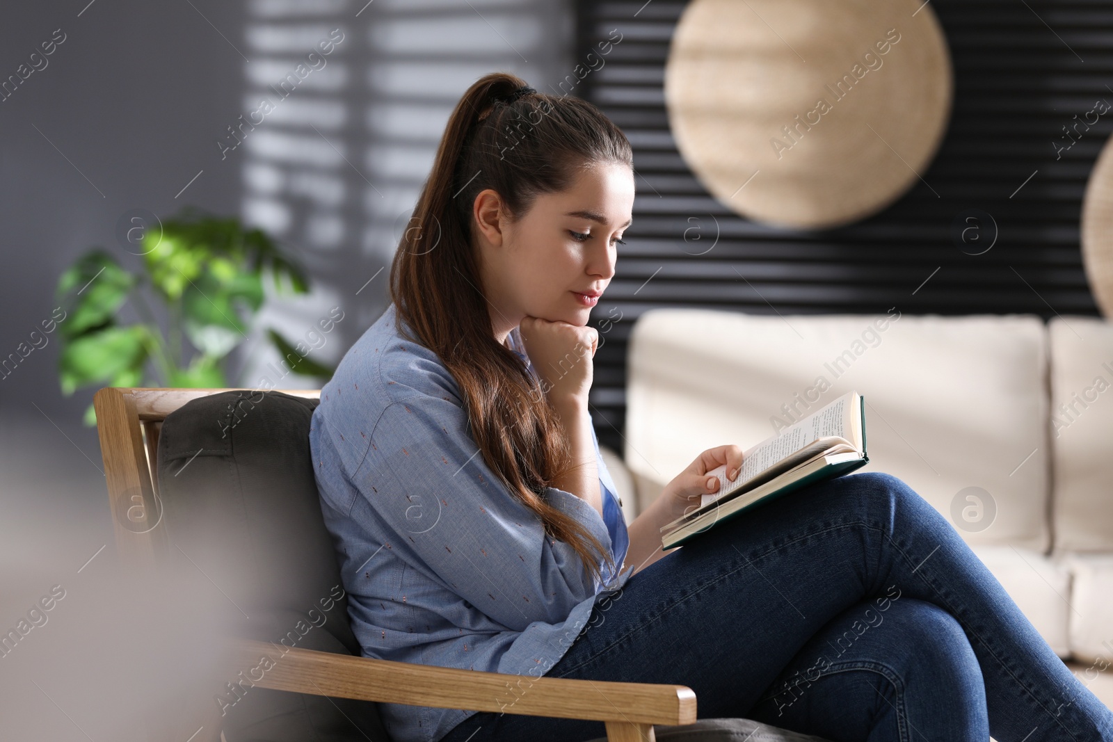 Photo of Young woman with book sitting in armchair at home