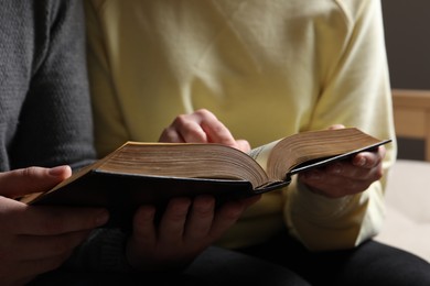 Photo of Couple sitting and reading holy Bible indoors, closeup