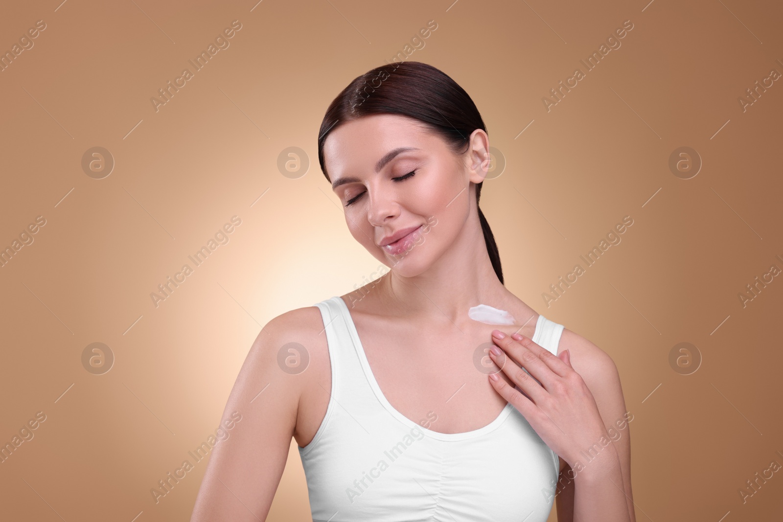 Photo of Beautiful woman with smear of body cream on her neck against light brown background