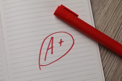Photo of School grade. Red letter A with plus symbol on notebook paper and marker on table, top view