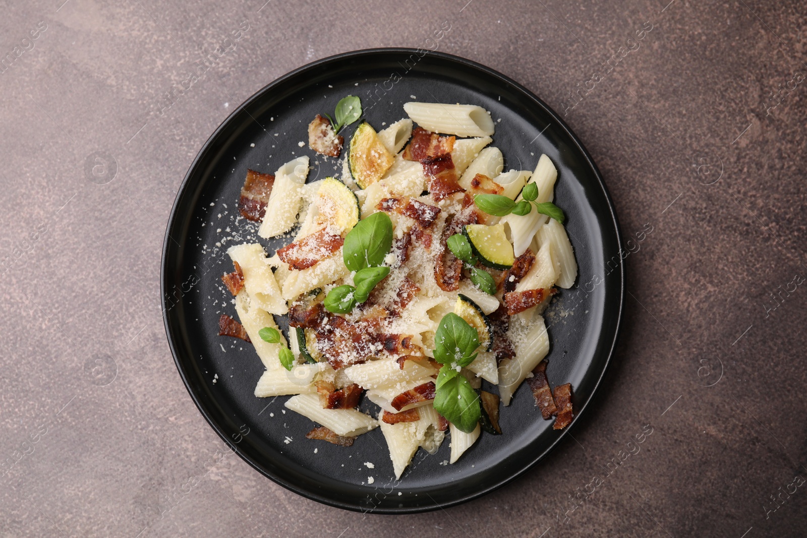 Photo of Tasty pasta with bacon and basil on brown table, top view