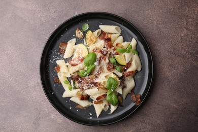 Tasty pasta with bacon and basil on brown table, top view