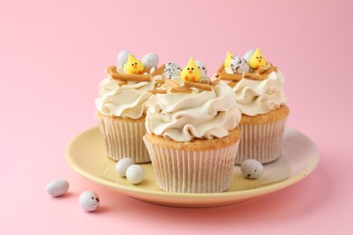 Tasty Easter cupcakes with vanilla cream and candies on pink background