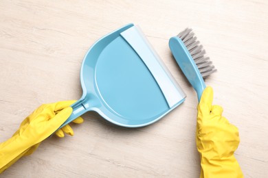 Photo of Woman in gloves sweeping wooden floor with plastic whisk broom and dustpan, top view