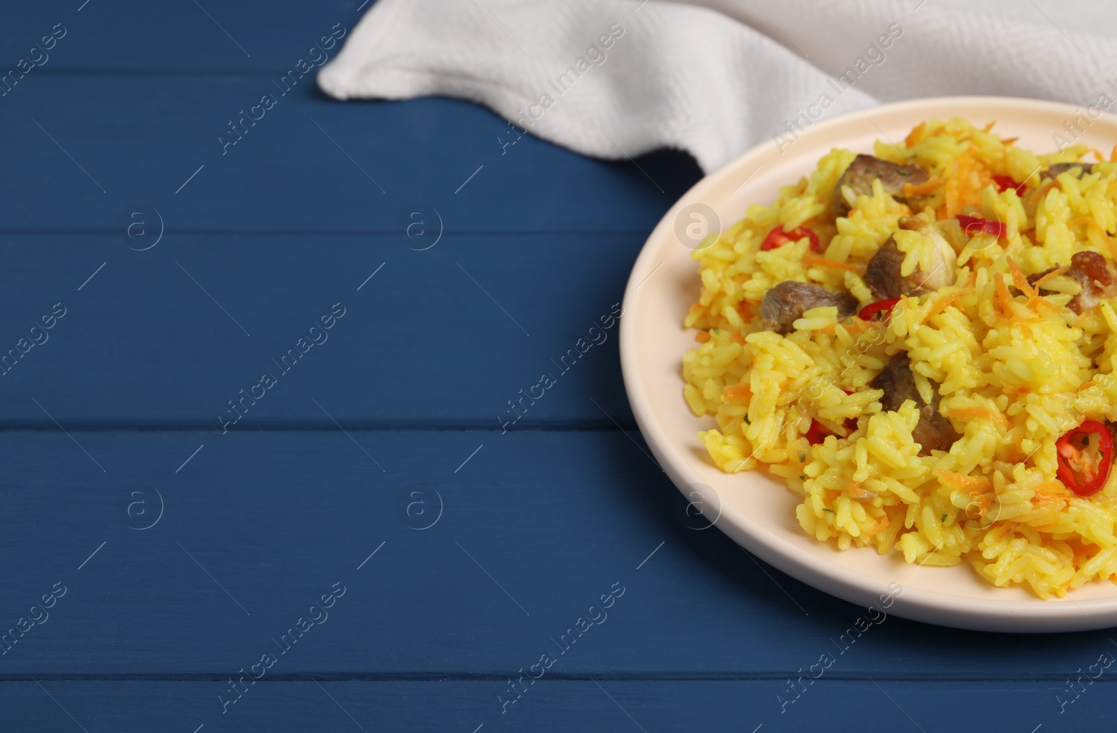 Photo of Delicious pilaf with meat on blue wooden table. Space for text