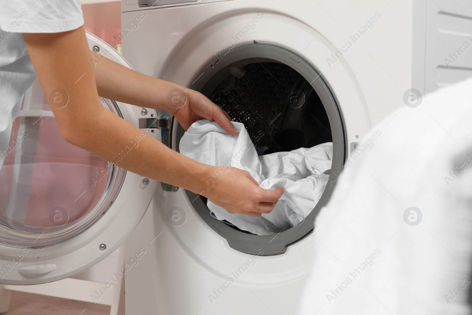 Photo of Woman taking laundry out of washing machine indoors, closeup